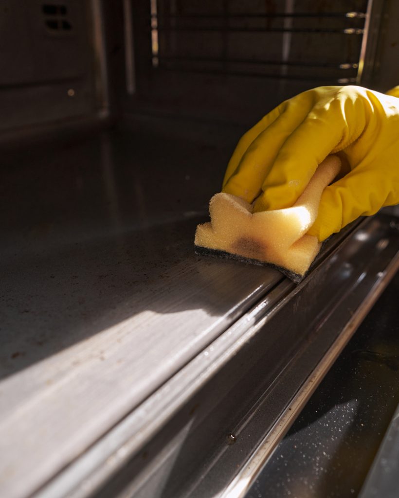 Cropped photo of hand in rubber glove wiping inside of oven with sponge
